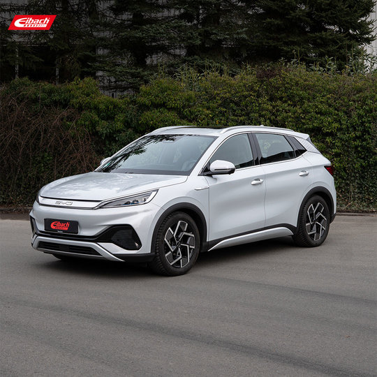 Ein silberner BYD Atto 3 SUV parkt auf einer Straße vor grünen Büschen und Bäumen. Oben links und auf dem Nummernschild ist der Eibach-Schriftzug zu sehen. Es ist bewölkt. Ein silberner BYD Atto 3 SUV parkt auf einer Straße vor grünen Büschen und Bäumen. Oben links und auf dem Nummernschild ist der Eibach-Schriftzug zu sehen. Es ist bewölkt.