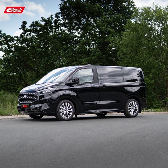 A black minivan is parked on a road with green trees and bushes in the background. The Eibach logo is visible in the upper left corner of the image. A black minivan is parked on a road with green trees and bushes in the background. The Eibach logo is visible in the upper left corner of the image.