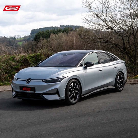 Eine silberne Elektrolimousine von Volkswagen parkt auf einer Straße mit Bäumen, Hügeln und bewölktem Himmel im Hintergrund. Das Auto besticht durch sein elegantes, modernes Design und dunkle Akzente an Rädern und Dach. Das Eibach-Logo befindet sich in der oberen linken Ecke. Eine silberne Elektrolimousine von Volkswagen parkt auf einer Straße mit Bäumen, Hügeln und bewölktem Himmel im Hintergrund. Das Auto besticht durch sein elegantes, modernes Design und dunkle Akzente an Rädern und Dach. Das Eibach-Logo befindet sich in der oberen linken Ecke.