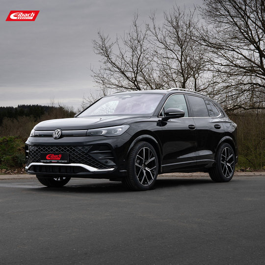 Ein schwarzer Volkswagen SUV steht auf einer befestigten Fläche im Freien, im Hintergrund Bäume und bewölkter Himmel. Das Auto ist mit sportlichen Felgen ausgestattet, und das Eibach-Logo ist in der oberen linken Ecke und auf dem vorderen Nummernschild zu sehen.