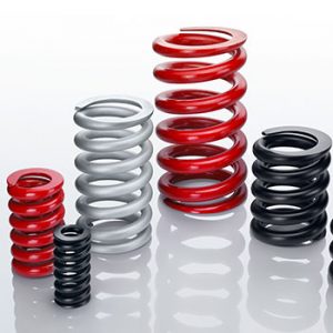 Eine Gruppe unterschiedlich großer Druckfedern in den Farben Rot, Grau und Schwarz, die aufrecht auf einer reflektierenden weißen Oberfläche stehen.