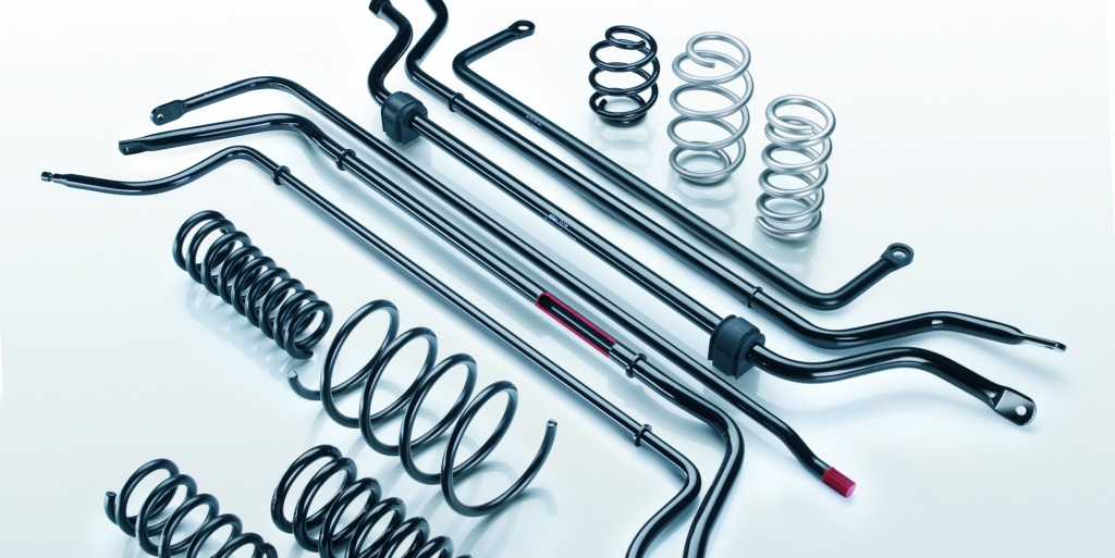 Eine Vielzahl schwarzer Metallfedern und Stabilisatoren für Autos, die ordentlich auf einer weißen Fläche angeordnet sind, wobei einige Schraubenfedern aufrecht stehen und andere liegen.