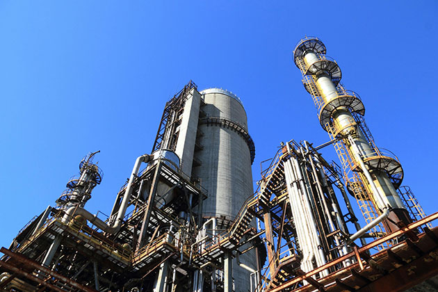 Industriekomplex mit hohen Metallstrukturen, Rohren und Türmen vor einem klaren blauen Himmel; typisch für die Industrie, möglicherweise eine Raffinerie oder ein Chemiewerk, in dem industriefedernde Einsatzbereiche wesentlich sind.