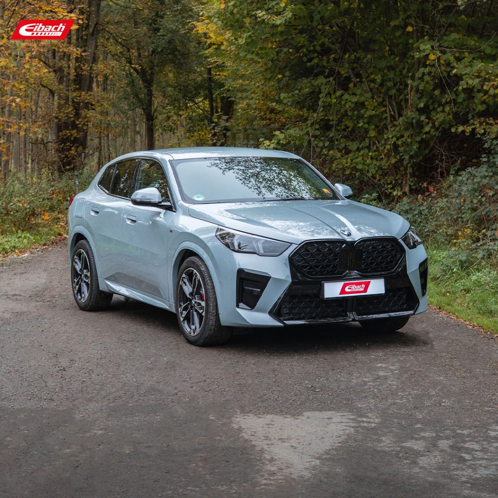 Ein silberner BMW X2 SUV ist auf einem Waldweg mit Bäumen und Herbstlaub im Hintergrund geparkt. Das Auto hat ein sportliches Styling und einen Eibach Schriftzug auf dem Nummernschild und in der oberen linken Ecke. Ein silberner BMW X2 SUV ist auf einem Waldweg mit Bäumen und Herbstlaub im Hintergrund geparkt. Das Auto hat ein sportliches Styling und einen Eibach Schriftzug auf dem Nummernschild und in der oberen linken Ecke.