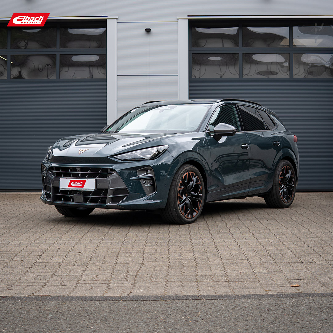 Ein dunkelgrüner Cupra-SUV steht auf einer gepflasterten Fläche vor modernen, grauen Garagentoren. Das Auto hat sportliche schwarze Felgen und ein Eibach-Kennzeichen. Das Eibach-Logo ist in der oberen linken Ecke zu sehen.